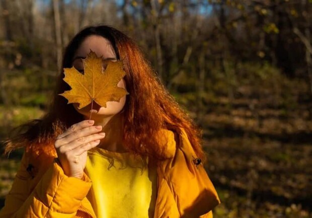 Девушка держит в руке осенний листок. 