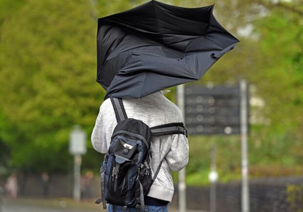 Чоловік іде з парасолькою під час сильного вітру. 